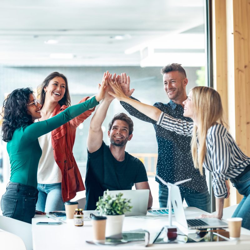 Shot of group of successful smart business team celebrating good job while holding up their right hands on coworking place.